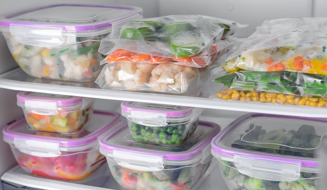 Behälter und Plastikbeutel mit gefrorenem Gemüse im Kühlschrank
