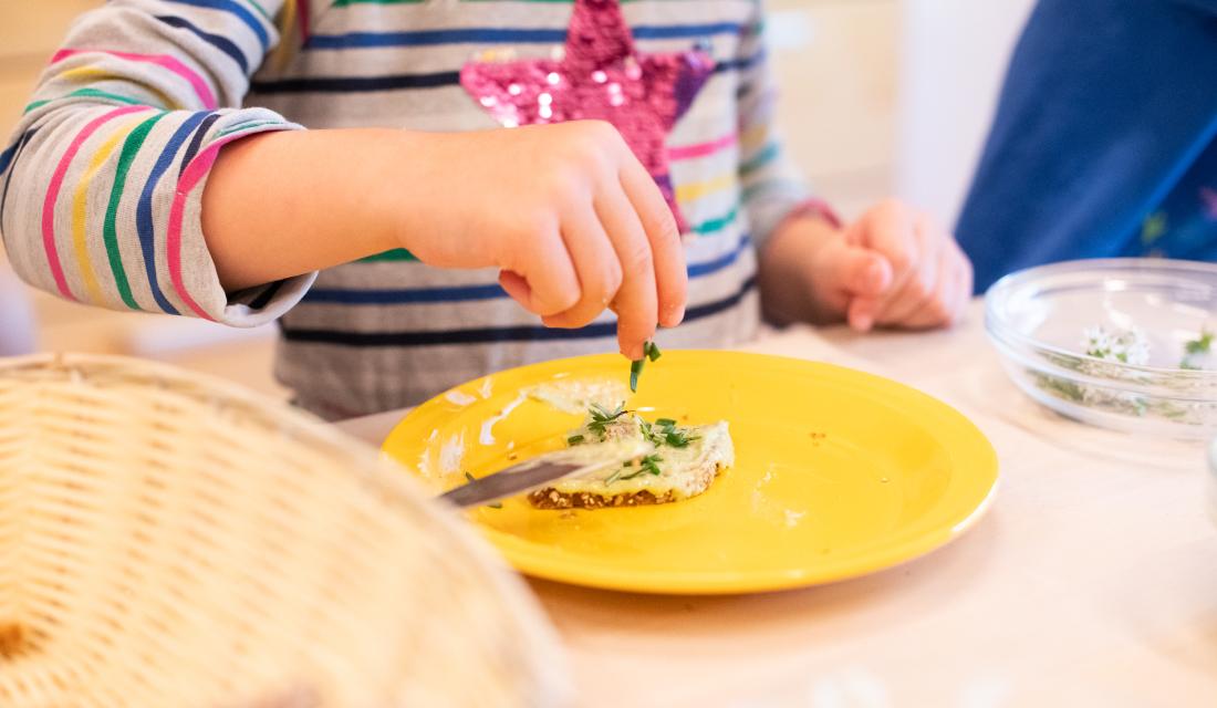 Ernährungsbildungsaktion mit Kindern. Brote schmieren und mit Kräutern belegen.