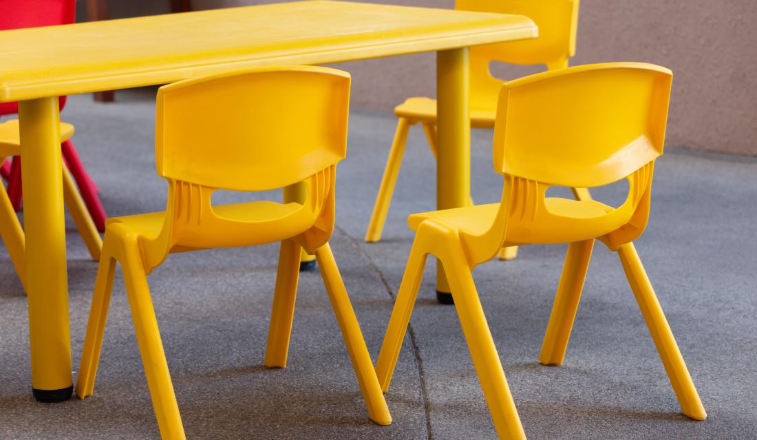 Ein gelber Kinderstuhl aus Plastik steht neben einem anderen gelben Plastikstuhl