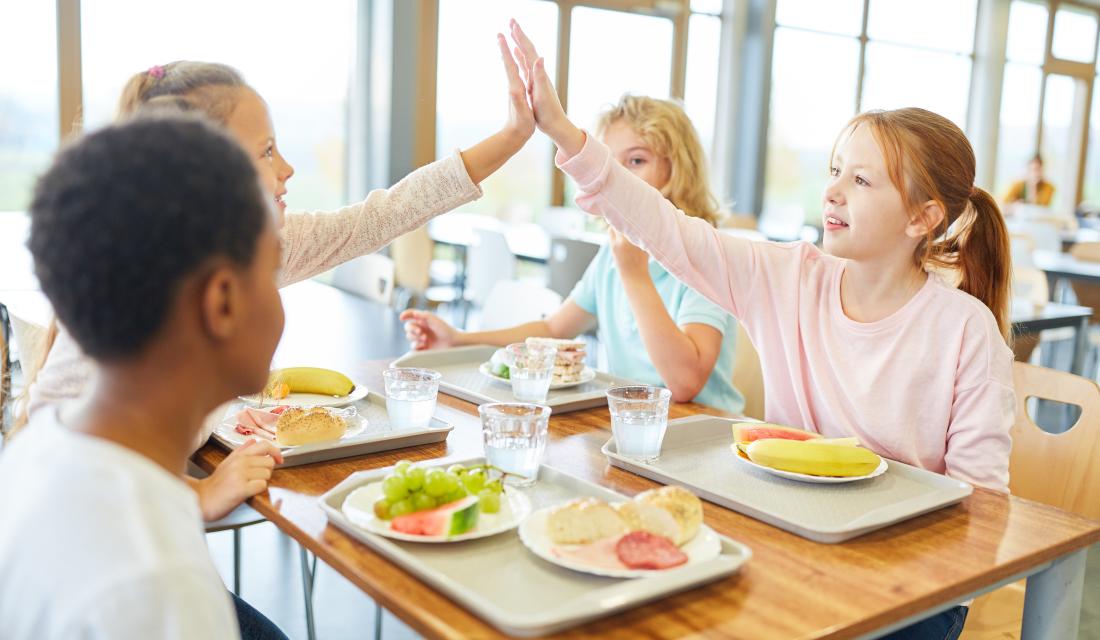 Glückliche Kinder in der Mensa geben sich selbst ein High Five
