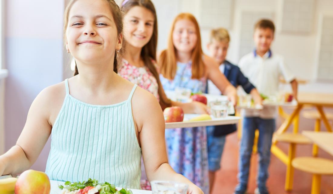 Lächelnde Studenten stehen in der Schlange und halten Tabletts mit Essen
