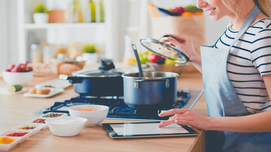 Junge Frau benutzt einen Tablet-Computer zum Kochen in ihrer Küche