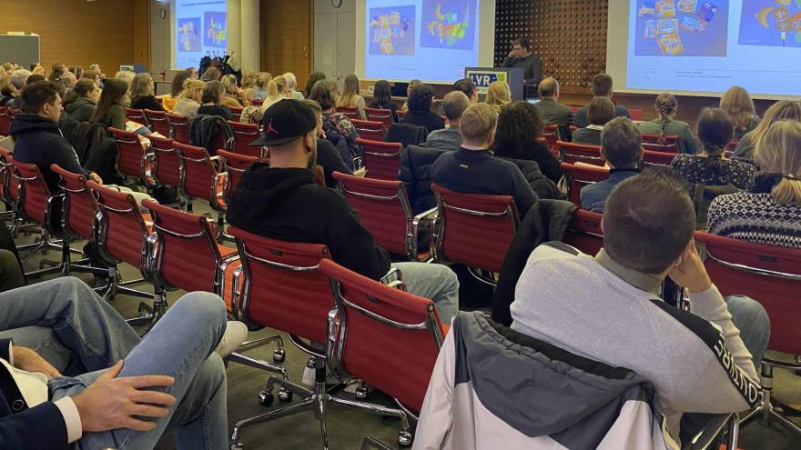 Personen im Saal hören einem Vortrag.
